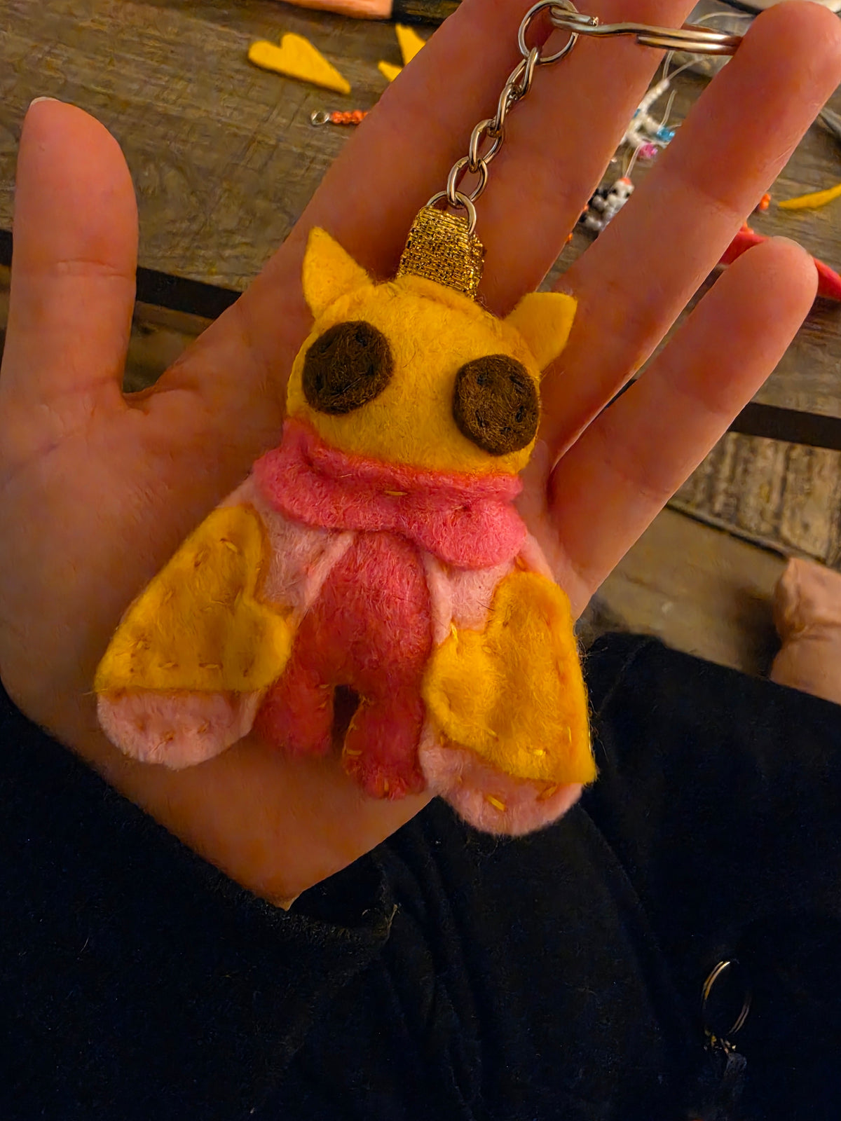 Handmade felt Rosy Maple Moth keychain held in palm, showing yellow wings and pink body